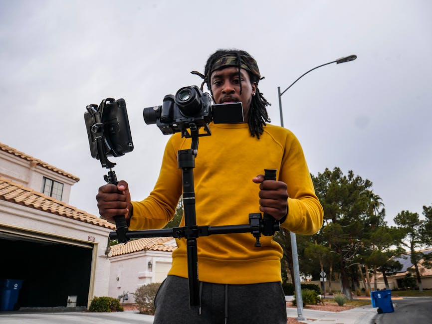 A young man operates a camera with a stabilizer outdoors, showcasing modern filming techniques.